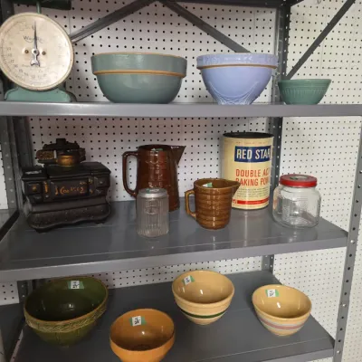 Sale Photo Thumbnail #35: Collection of vintage kitchenware on shelving, including mixing bowls, a vintage Way-Rite kitchen scale, a stove-shaped cookie jar, brown glazed pitchers, and a Red Star baking powder tin.