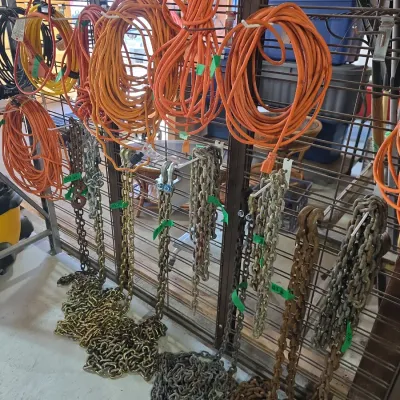 Sale Photo Thumbnail #123: Assorted heavy-duty extension cords and metal tow chains displayed on a wire rack setup, appearing in used, working condition.