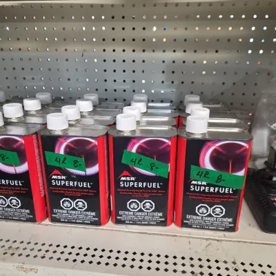 Sale Photo Thumbnail #136: Multiple metal quart cans of MSR Superfuel liquid camp stove fuel arranged on pegboard shelving.