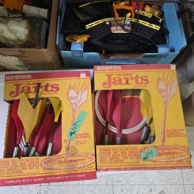 Sale Photo Thumbnail #49: Two vintage Regent "Slider" Jarts lawn dart sets in their original boxes, along with a box of electric race track components stored on a shelf.