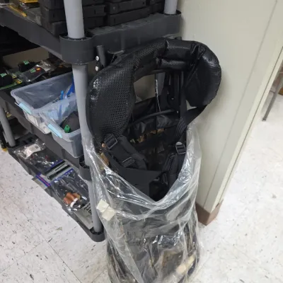 Sale Photo Thumbnail #81: Black external frame backpack system partially wrapped in plastic, displayed alongside utility shelves holding tactical accessories.