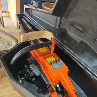 Sale Photo Thumbnail #124: Vintage Echo 300EVL orange gas-powered chainsaw housed in its original black molded plastic carrying case.