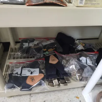 Sale Photo Thumbnail #56: Assorted work accessories and outdoor gear, including CLC heavy-duty suspenders, small leather sheaths, and emergency matches, displayed on plastic shelving.