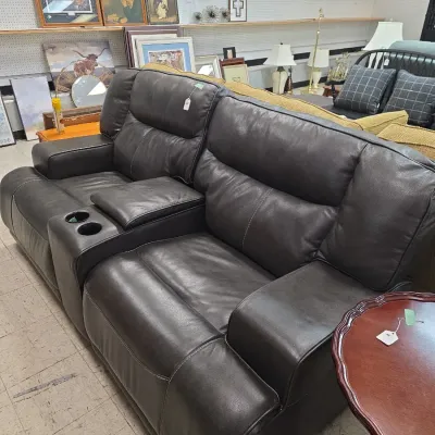 Sale Photo Thumbnail #21: Contemporary dark brown leather reclining loveseat with a center console featuring cupholders and storage, displayed alongside various home decor and furniture.