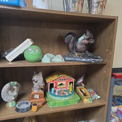 Sale Photo Thumbnail #64: Shelves containing eclectic collectibles, including a vintage Fisher-Price 'Farmer in the Dell' music box, cast metal squirrel figurine, small wolf head bust, and polished ammonite fossil specimen.
