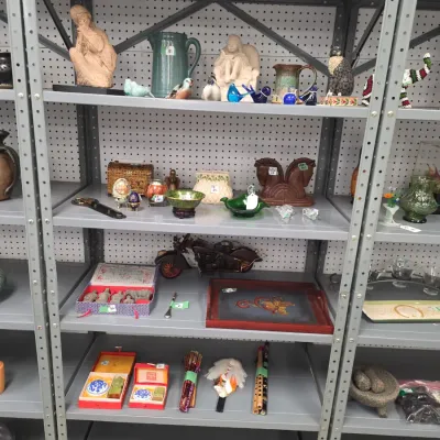 Sale Photo Thumbnail #25: Grey metal shelving unit display filled with various collectibles, including ceramic figurines, glass bird ornaments, horse head bookends, a toy motorcycle, and boxed Asian decorative sets.