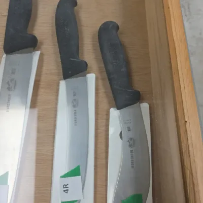 Sale Photo Thumbnail #75: Trio of Victorinox Forschner commercial kitchen knives with ergonomic black Fibrox handles, each in protective white plastic sheaths inside a display case.
