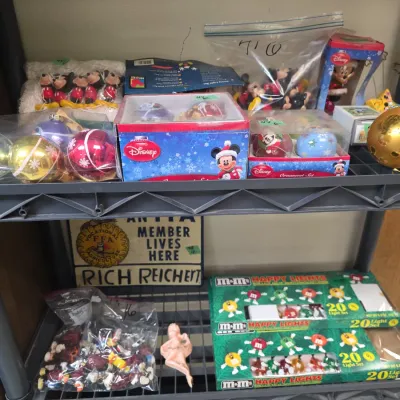 Sale Photo Thumbnail #65: Collection of vintage holiday decorations including Disney Mickey Mouse ornaments, M&M's string lights in original boxes, and a personalized FFA metal member sign on a plastic shelving unit.