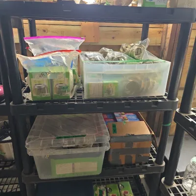 Sale Photo Thumbnail #122: Black plastic shelving unit organized with canning supplies, including plastic bins filled with jar lids, boxed canning accessories, and storage totes.
