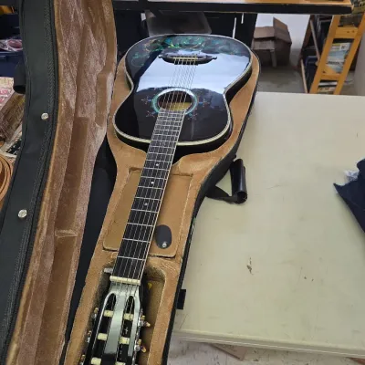 Sale Photo Thumbnail #45: Black acoustic guitar featuring colorful inlay artwork on the body, presented inside a tan velvet-lined hard case.