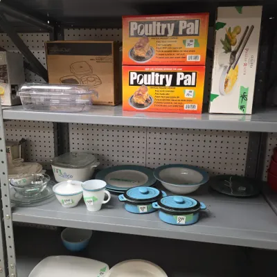 Sale Photo Thumbnail #39: Metal shelving unit displayed with assorted kitchenware, including boxed Poultry Pal vertical roasters, a Cuisipro potato ricer, blue ceramic mini Dutch ovens, and vintage CorningWare dishes.