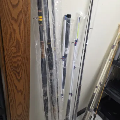 Sale Photo Thumbnail #69: Collection of modern fishing rods standing upright against a wall, mostly stored in clear protective plastic sleeves.
