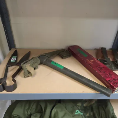 Sale Photo Thumbnail #61: Vintage military entrenching tool with canvas sheath, displayed alongside hand shears and boxed collectibles on metal shelving.
