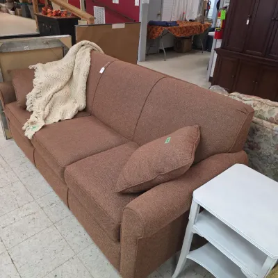 Sale Photo Thumbnail #13: Brown upholstered three-cushion sofa featuring matching accent pillows, a cream fringe throw blanket, and an adjacent white nightstand.