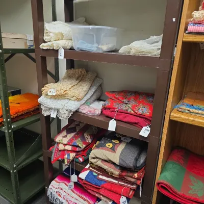 Sale Photo Thumbnail #32: Brown plastic shelving unit displayed with assortment of vintage baby blankets, quilts, knit shawls, and textiles labeled "Baby Land".