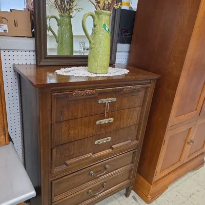 Sale Photo Thumbnail #20: Vintage dark wood tall chest of drawers featuring decorative carved accents, mixed hardware pulls, and a matching framed wall mirror mounted above.