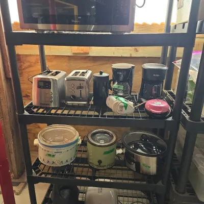 Sale Photo Thumbnail #121: Black plastic shelving unit holding various small kitchen appliances, including a Whirlpool microwave, two-slice toasters, drip coffee makers, slow cookers, and a hand mixer.