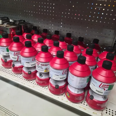 Sale Photo Thumbnail #133: Large stock of red Coleman premium blend fuel canisters arranged on retail shelving.