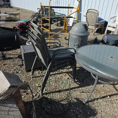 Sale Photo Thumbnail #142: Assorted outdoor patio furniture and garden items, including a round glass-top table, stacked mesh chairs, plastic lawn chairs, scaffolding, and a metal trash receptacle.