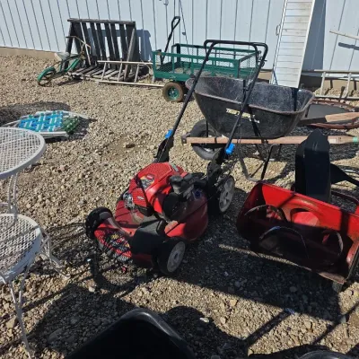 Sale Photo Thumbnail #144: Outdoor lawn care equipment including a red Toro walk-behind lawn mower, a wheelbarrow, a green utility wagon, and a snow blower attachment.