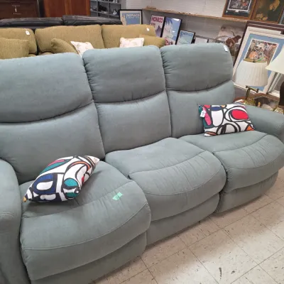 Sale Photo Thumbnail #7: Contemporary light blue upholstered three-seat reclining sofa paired with colorful abstract-pattern throw pillows.
