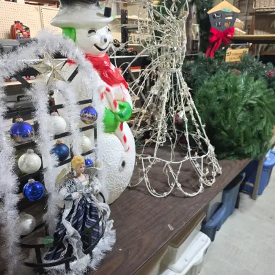 Sale Photo Thumbnail #130: Collection of Christmas decorations including a vintage plastic snowman blow mold, light-up wire angel frame, artificial wreaths, and an ornament display stand with glass baubles.