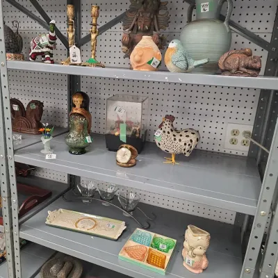 Sale Photo Thumbnail #24: Collection of eclectic home decor displayed on metal shelving, including brass candlesticks, a pottery bird figurine, a ceramic rooster, glassware, and a stone molcajete.