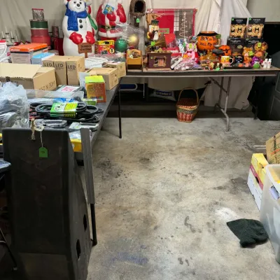 Sale Photo Thumbnail #35: Collection of holiday decorations and household goods on folding tables, including blow mold Christmas figures, Halloween decor, and boxed LED lights.