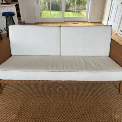 Sale Photo Thumbnail #9: Woven rattan sofa with cream-colored upholstery, featuring a clean-lined frame and matching seat and back cushions.