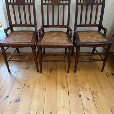 Sale Photo Thumbnail #49: Set of three antique dark wood dining chairs featuring carved spindle backs and cane seats.