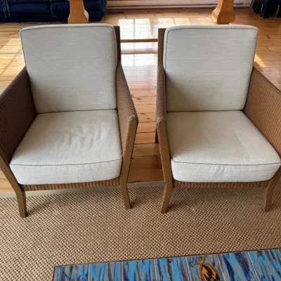 Sale Photo Thumbnail #10: Pair of modern outdoor woven armchair style patio chairs featuring brown wicker bases and off-white removable cushions.