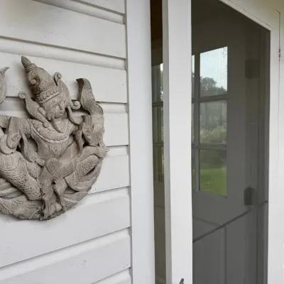 Sale Photo Thumbnail #7: Pair of vintage carved wood wall plaques depicting Southeast Asian deity figures mounted on an exterior siding wall.