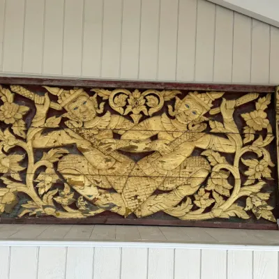 Sale Photo Thumbnail #24: Intricately hand-carved Southeast Asian giltwood wall panel depicting two mythological figures amid floral scrolls, featuring mirrored inlay details and showing vintage wear to the gold finish.