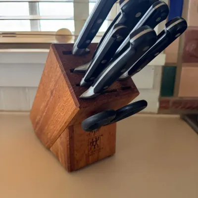 Sale Photo Thumbnail #47: J.A. Henckels kitchen knife set housed in a natural wooden counter block, including kitchen shears and assorted cutlery with black riveted handles.