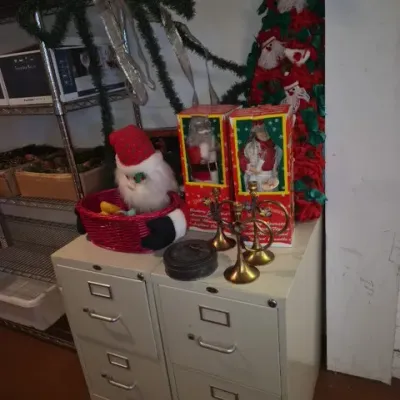 Sale Photo Thumbnail #152: Pair of two-drawer metal filing cabinets holding a collection of vintage Christmas decorations, including boxed animated figures, brass candleholders, and a Santa basket.