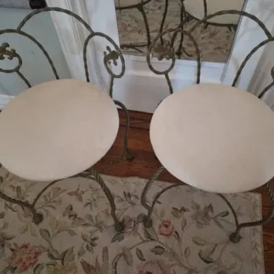 Sale Photo Thumbnail #54: Pair of vintage wrought iron vanity stools featuring twisted metal legs, fleur-de-lis accents, and cream upholstered round seats.