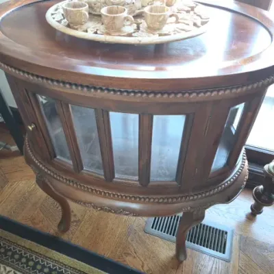 Sale Photo Thumbnail #24: Vintage oval wood tea cabinet with glass paneled doors, beaded trim, and cabriole legs, topped with a decorative marble espresso set.