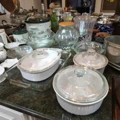 Sale Photo Thumbnail #126: Large collection of kitchenware and cookware, including CorningWare French White casseroles with glass lids, Pyrex baking dishes, clear glass storage jars, and metal pots.