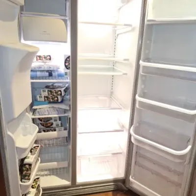 Sale Photo Thumbnail #145: Modern side-by-side refrigerator freezer with stainless steel finish, featuring illuminated interior glass shelves and door bins.