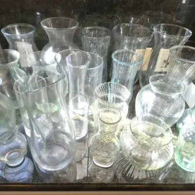 Sale Photo Thumbnail #136: Large collection of assorted clear glass vases, pitchers, and vessels in various shapes and sizes displayed on a dark countertop.