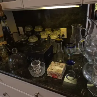 Sale Photo Thumbnail #130: Collection of glassware and kitchenware, including clear glass pitchers, canisters with lids, a small cloche, and a cobalt blue-rimmed glass.