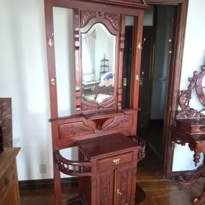 Sale Photo Thumbnail #31: Victorian-style carved mahogany hall tree featuring a central shaped mirror, brass coat hooks, integrated umbrella stands, and a lower cabinet with carved details.