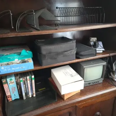 Sale Photo Thumbnail #140: Dark stained wooden hutch filled with various office supplies, media cases, wire organizers, and a small vintage CRT television.