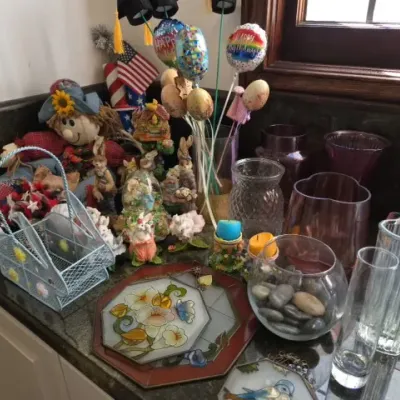 Sale Photo Thumbnail #137: Collection of seasonal decor, glass vases, rabbit figurines, a fabric scarecrow, and a floral stained-glass suncatcher arranged on a kitchen countertop.