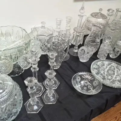 Sale Photo Thumbnail #123: Collection of clear pressed glass and cut crystal tableware including candlesticks, pitchers, covered jars, bowls, and serving platters arranged on a table.