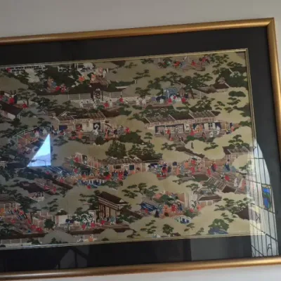 Sale Photo Thumbnail #69: Framed Japanese artwork depicting a detailed village scene, presented under glass with a dark mat and gold-tone frame.