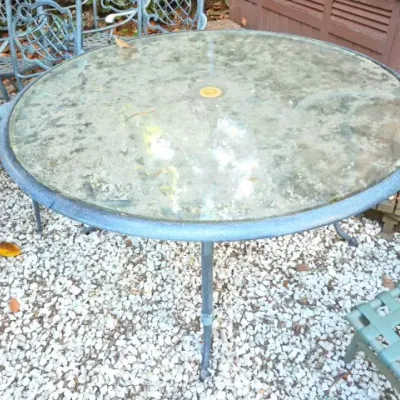 Sale Photo Thumbnail #172: Round outdoor patio table with a glass top, metal frame, and umbrella hole, accompanied by matching lattice-back chairs.