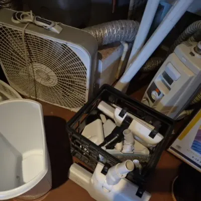 Sale Photo Thumbnail #182: A collection of household utility items including a square box fan, a vintage Electrolux canister vacuum cleaner with attachments, and a white trash bin.