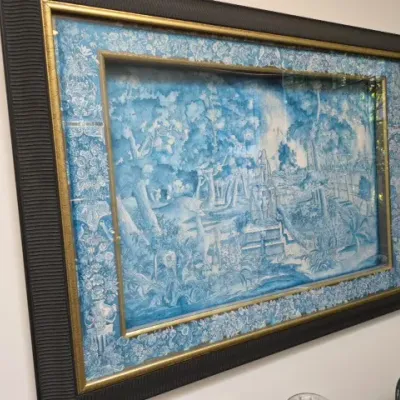 Sale Photo Thumbnail #61: Framed blue and white toile-style wall art featuring a landscape scene, set in a dark textured frame with gold trim.