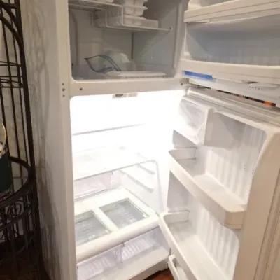 Sale Photo Thumbnail #146: White top-freezer refrigerator, clean and illuminated with open doors showing interior shelves and door bins.